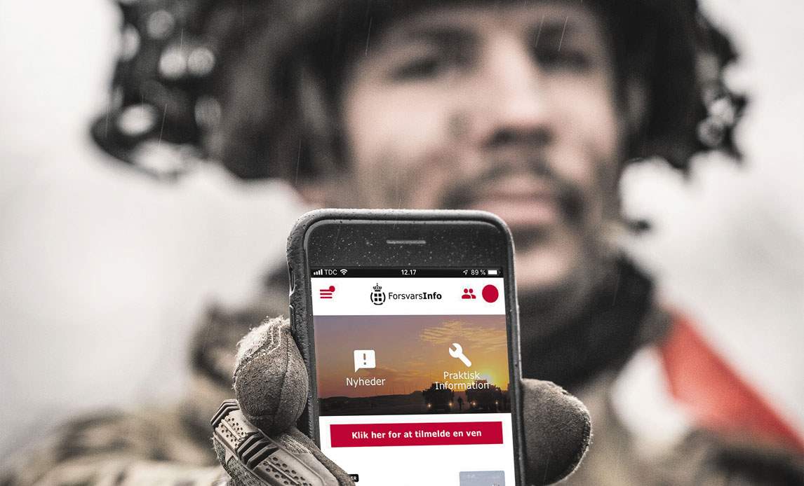 En soldat holder en mobiltelefon op i mod kameraet