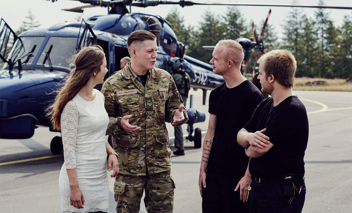 En ung kvinde i samtale med en soldat og to andre mænd foran en helikopter