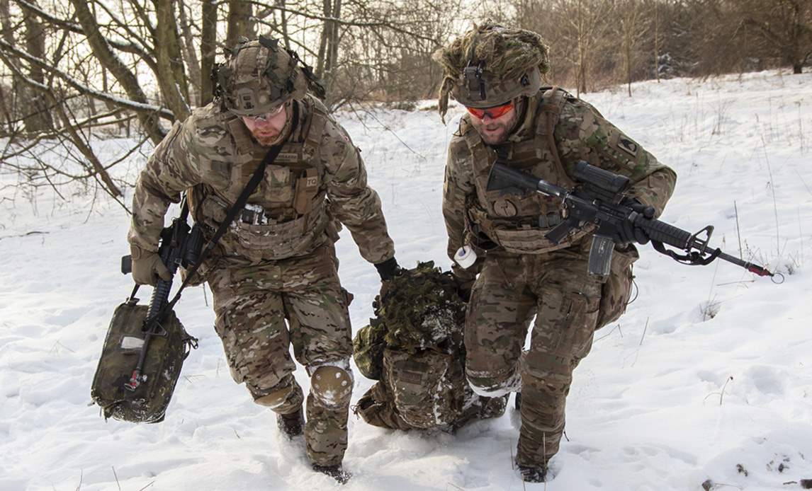 To soldater på øvelse i snevejr. De trækker en såret kollega efter sig.