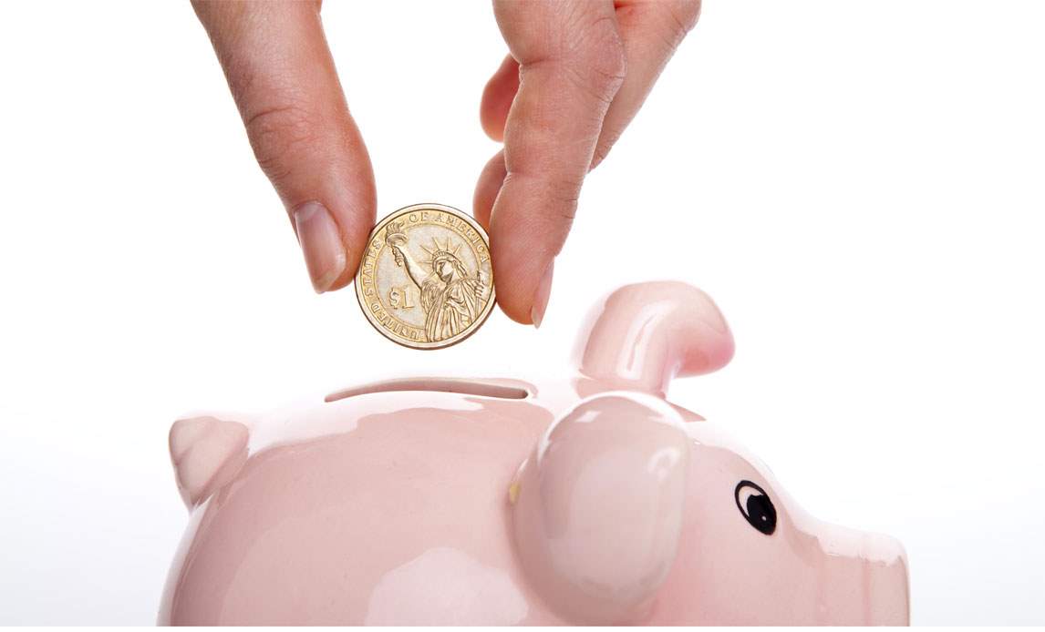 Stockfoto af en kvindehånd der putter en mønt i en lyserød sparegris