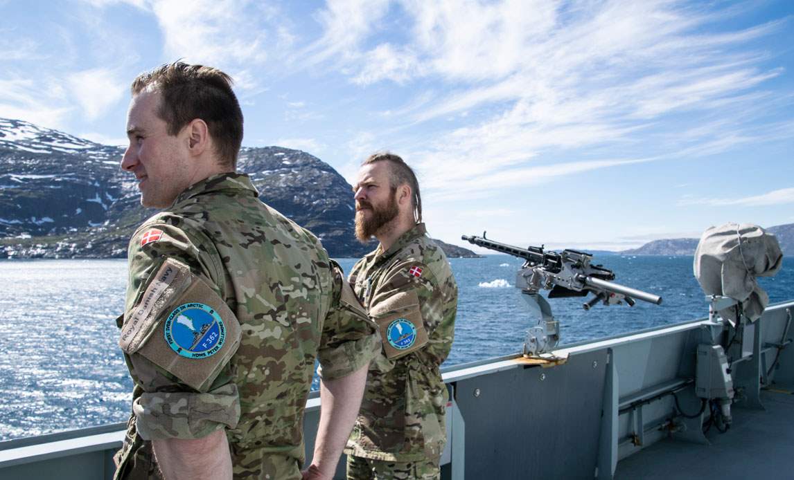 To soldater fra Søværnet står på dækket på fregatten Peter Willemoes, som sejler ud for Nuuk i Grønland.