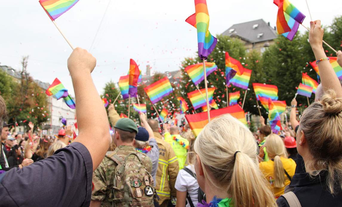 En gruppe medarbejdere, nogle i uniform, fra Forsvaret deltager i Copenhagen Pride Parade 2019 med regnbueflag og konfetti.