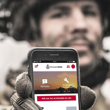 En soldat holder en mobiltelefon op i mod kameraet
