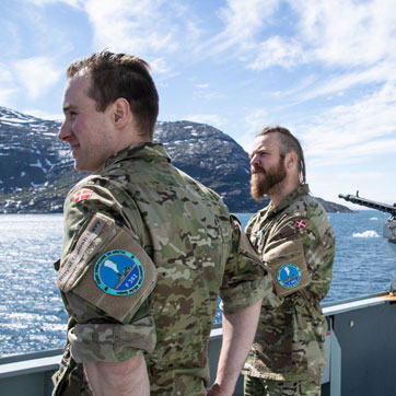 To soldater fra Søværnet står på dækket på fregatten Peter Willemoes, som sejler ud for Nuuk i Grønland.
