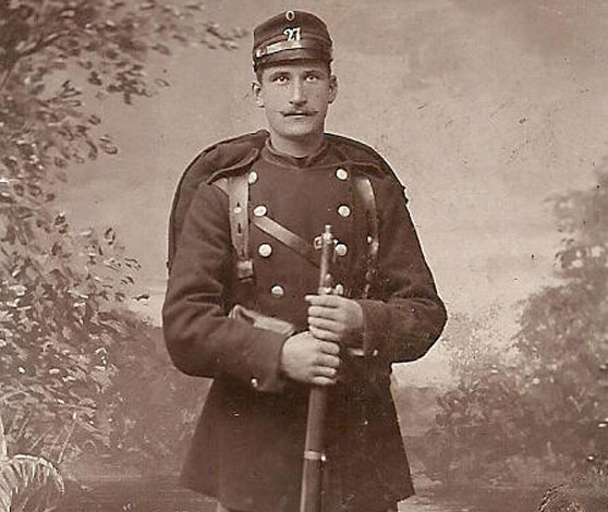 Portrætfoto af en ung værnepligtig i uniform og med gevær